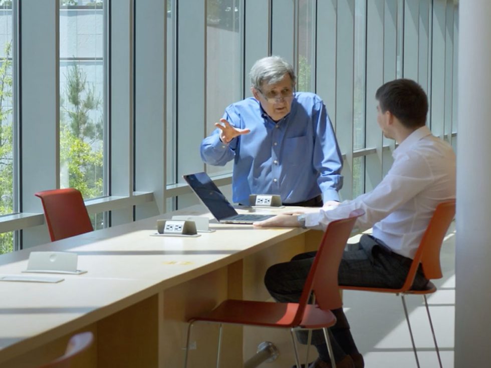 David Machlis, PhD leaning over a table while working with a student at Adelphi University