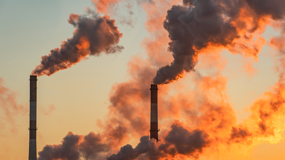 A smokestack at an industrial facility spews gray emissions into a late afternoon sky.