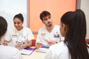 Nursing students studying together, woman on the left looking at her note cards, man on right looking off to the side, woman in ponytail sitting across from him.