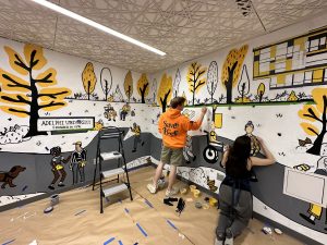 Two students working on painting a mural