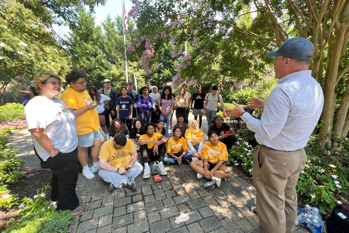 Students and FCAP members gathered in garden area, man in baseball cap facing them leading discussion.