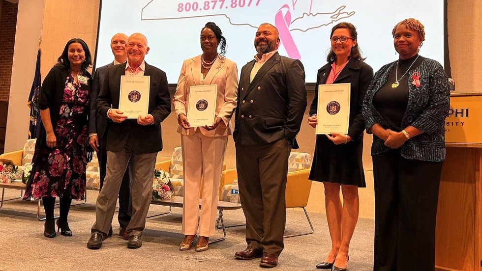 Seven people onstage, three holding certificates. Projected behind them is the state of New York in pink with the phone number 800.877.8077