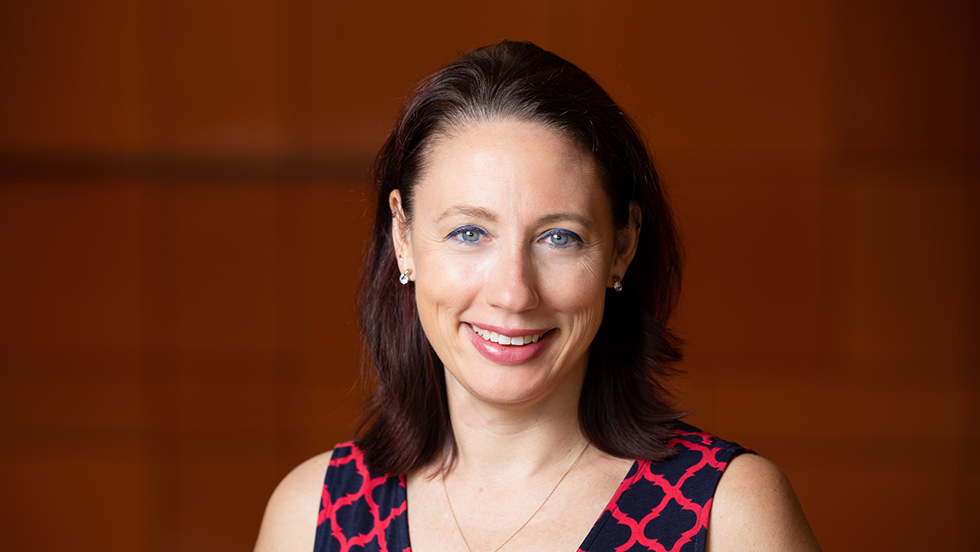 Beth Counselman Carpenter smiles for the camera, wearing a black dress with a red pattern, along with a pendant.