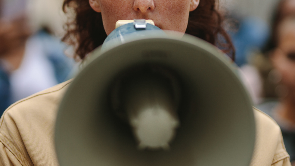 A close-up of a protestor with a bullhorn to his mouth. Behind him is a line of other protestors.