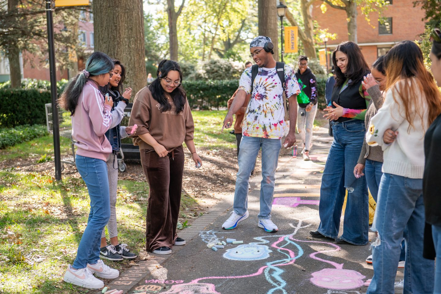 A group of students are smiling and admiring a chalk drawing on the ground.