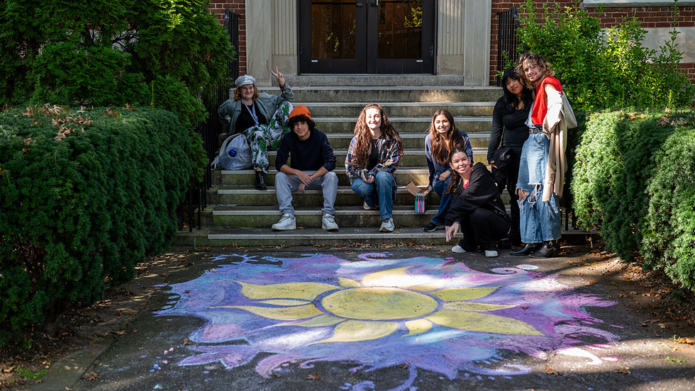 Students sitting outside of Blodgett Hall with large chalk artwork of a sunflower on the sidewalk