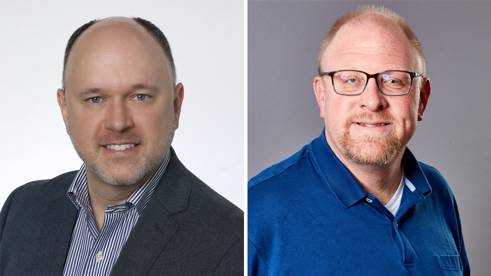 A white man wearing a striped button-down shirt and jacket (On the left). A white man with mustache and beard, wearing glasses and a blue shirt (On the right).