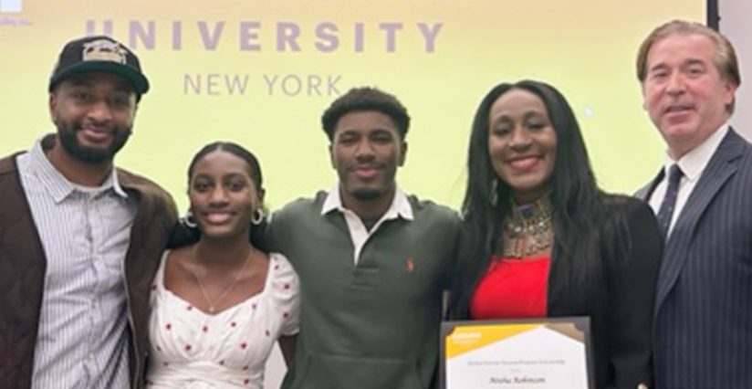 Atisha Robinson holds her award certificate. Her partner is on her left, while three of her children—a two young men and a young woman—are at her right. The Adelphi logo is projected onto a screen that stands behind them.