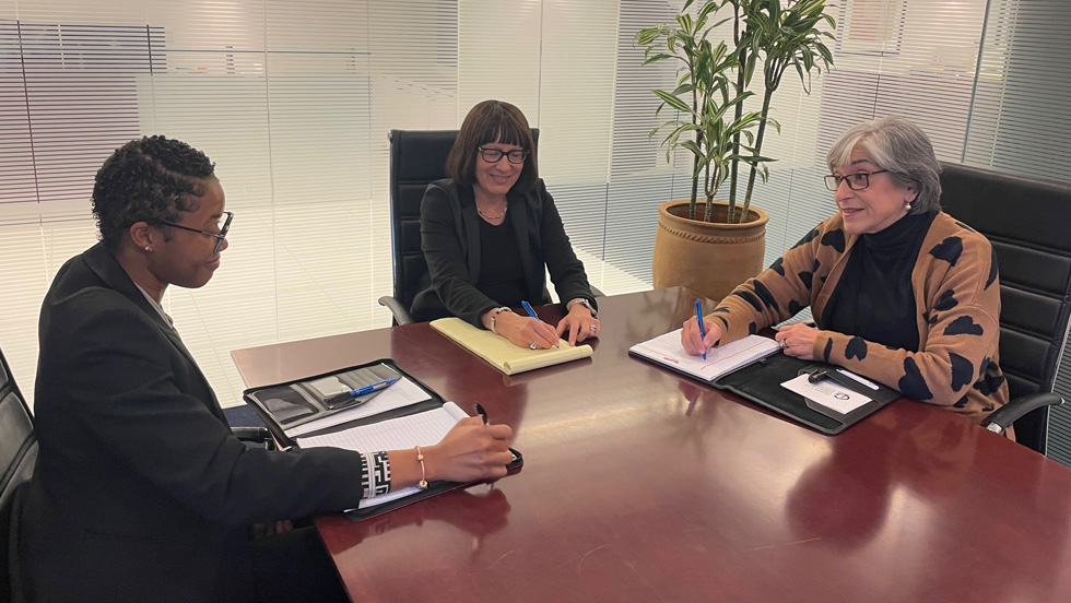  A young Black woman and two older white women at an office table