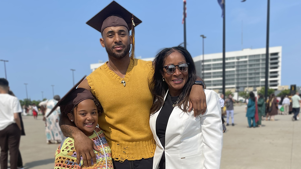 Chad Williams, wearing his mortarboard and with his arms around his daughter and mother, outside after the 2023 Commencement ceremony.