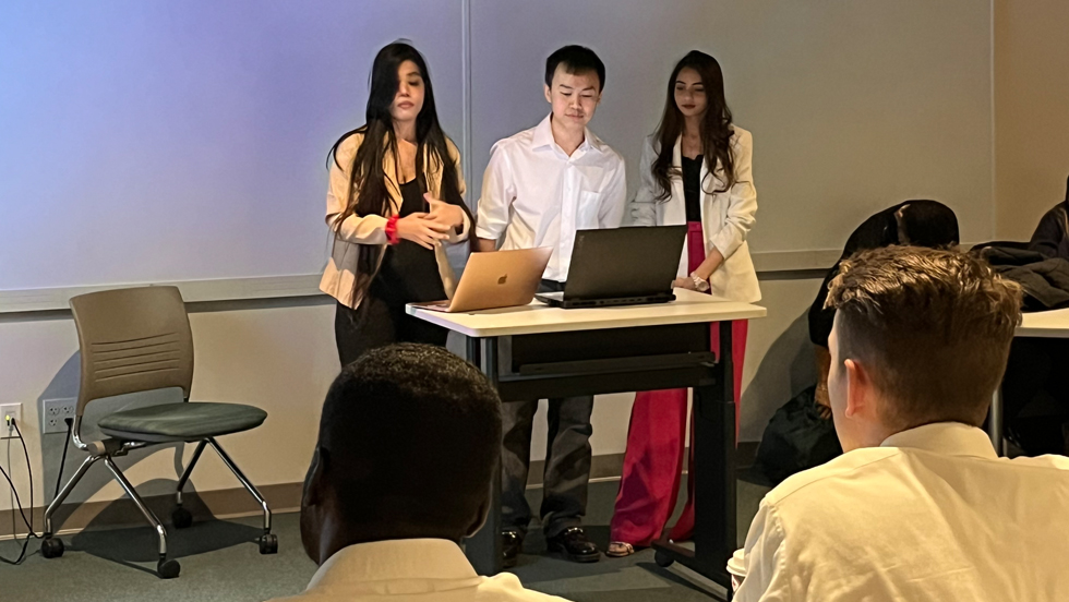 Three Adelphi Students standing at front of classroom and presenting. 