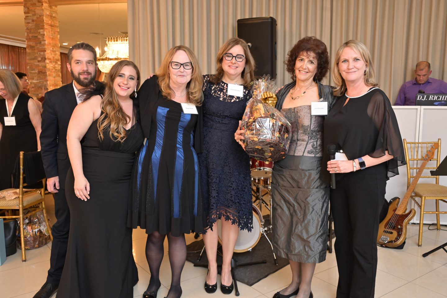 Five women, one holding a gift basket, and one man standing together