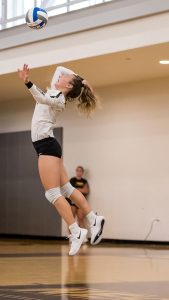 Yonker jumps high off the court to serve the ball in a league volleyball match.