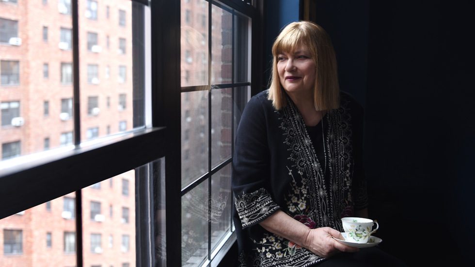 A woman sits with a cup of tea and gazes out a window.