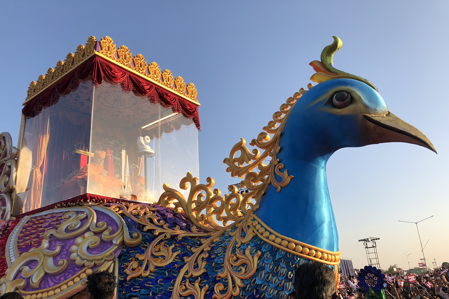 Large decorated bird acts as parade float. A man can be seen in a clear box on top of the bird's body.