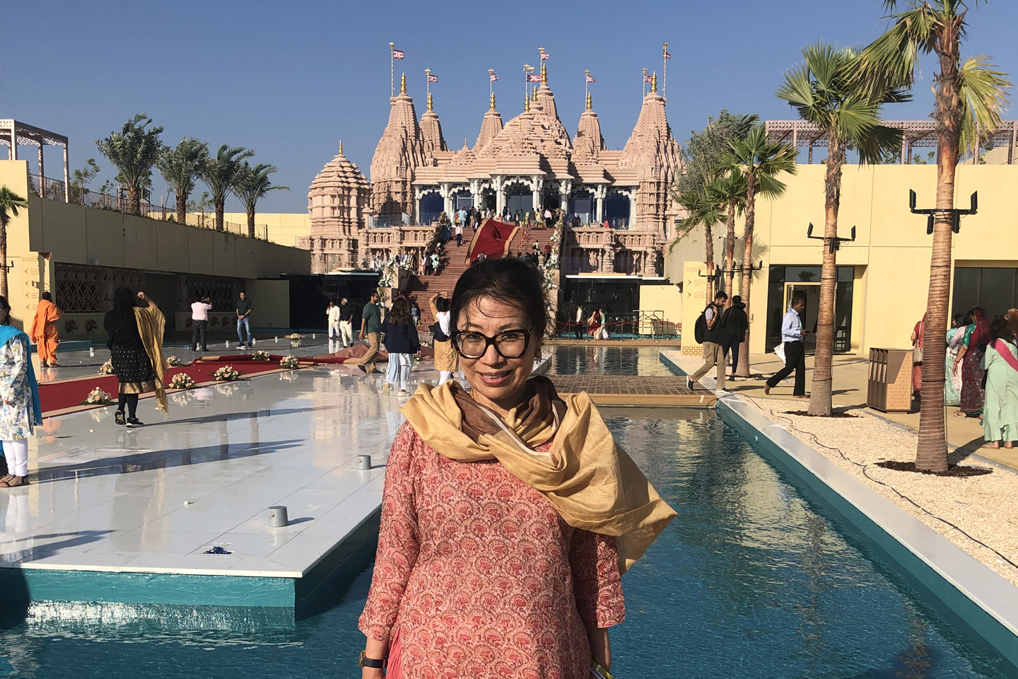 Professor Hanna Kim wearing large red framed glasses stands in front of a pool of water. In the background is a large temple.