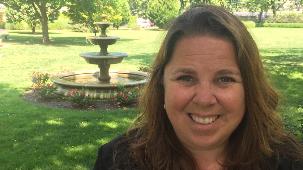 Smiling woman with long brown hair standing in front of a fountain