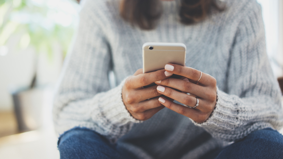 Woman from the neck down holds a cellphone in her hands.