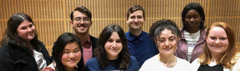 Eight students are standing in a group smiling at the camera