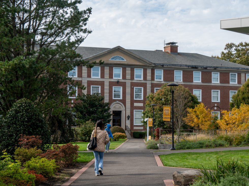 A student walks on the path toward Levermore Hall at Adelphi University