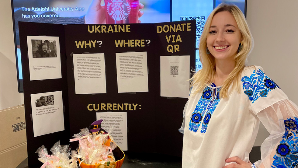 Tetyana Tomjuk, international student from Ukraine, with long blonde hair and a pink ruffled shirt in a dark background