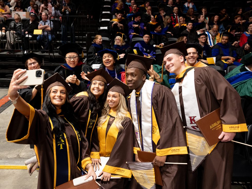  A group of five graduates posing with faculty at Adelphi's 2024 Commencement ceremony.