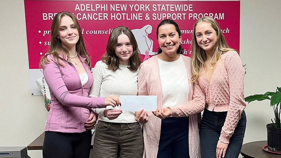 Adelphi Breast Cancer Program Receives Grant from Manhasset Junior Coalition - Four women smiling and holding a check in front of a pink banner