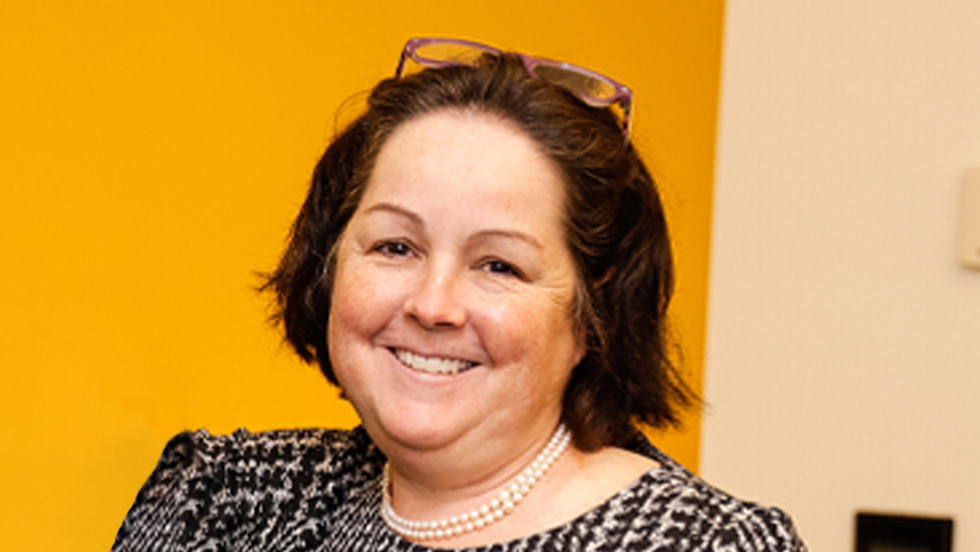 A smiling woman with brown hair and her eyeglasses placed on her head, wearing a black-and-white top 