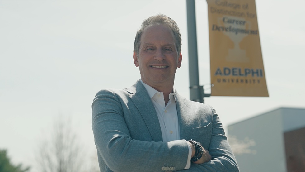 A man wearing a light blue blazer standing outside with his arms crossed and looking at the camera.