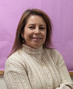 A woman wearing a cozy sweater in front of a purple wall