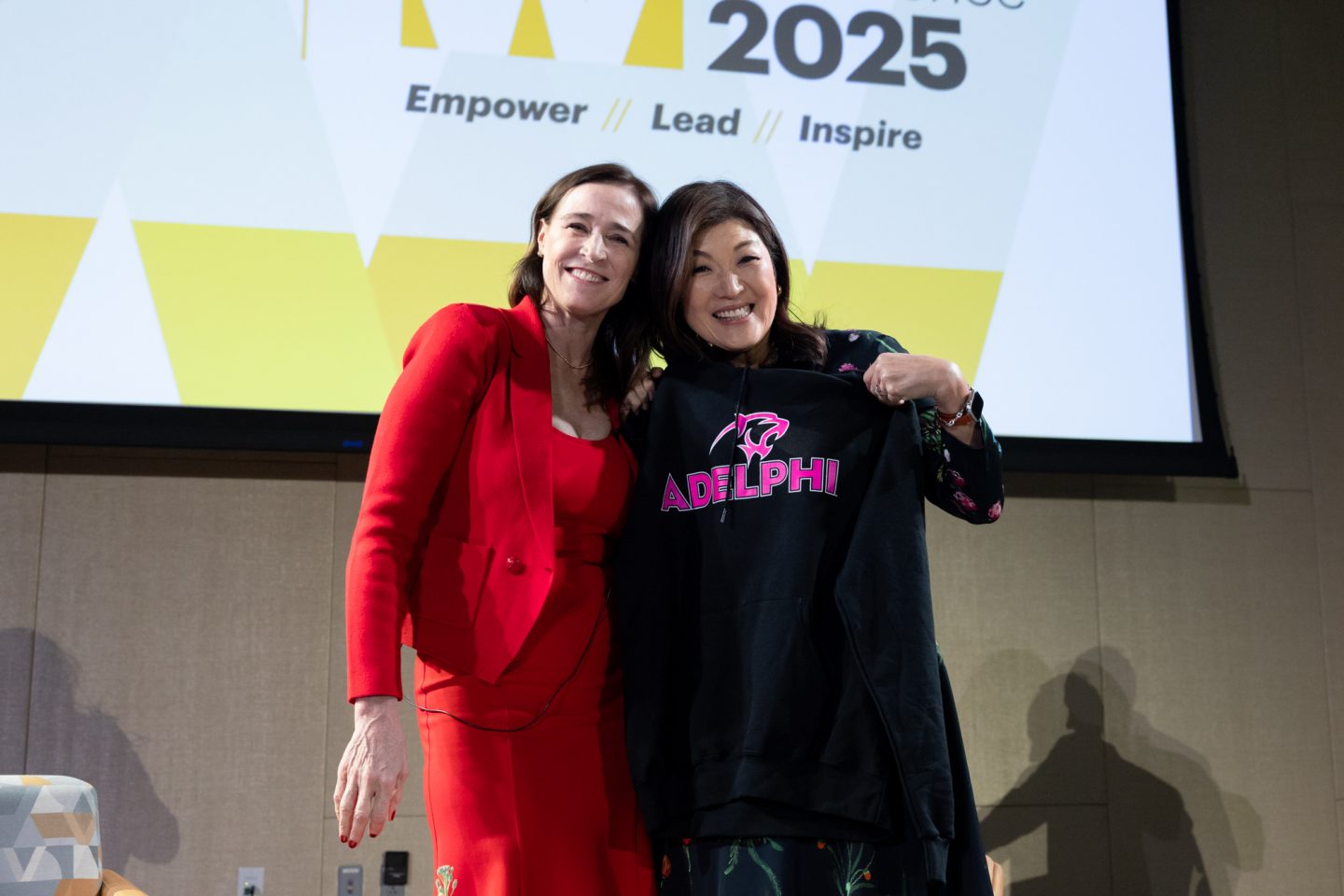 President Christine Riordan and JuJu Chang share a hug. Chang holds an Adelphi tee.