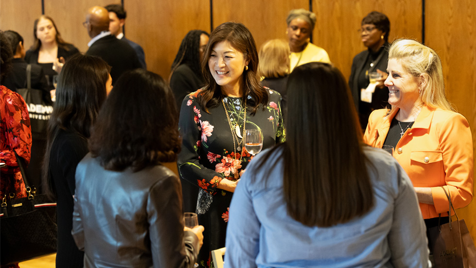 Emmy-winning co-anchor JuJu Chang chats and smiles with a large group of women attendees at the Conference