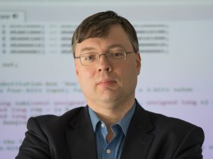 A professor in front of a white board with glasses.