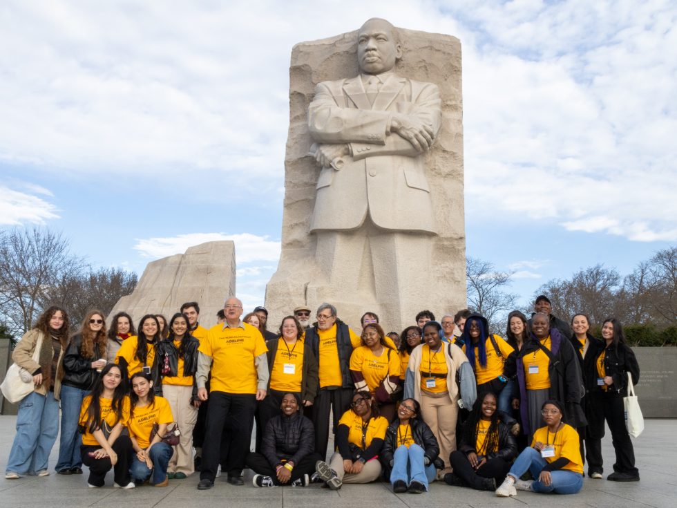 A group of about 25 students, faculty and administrators stand before the Martin Luther King Jr. Memorial.