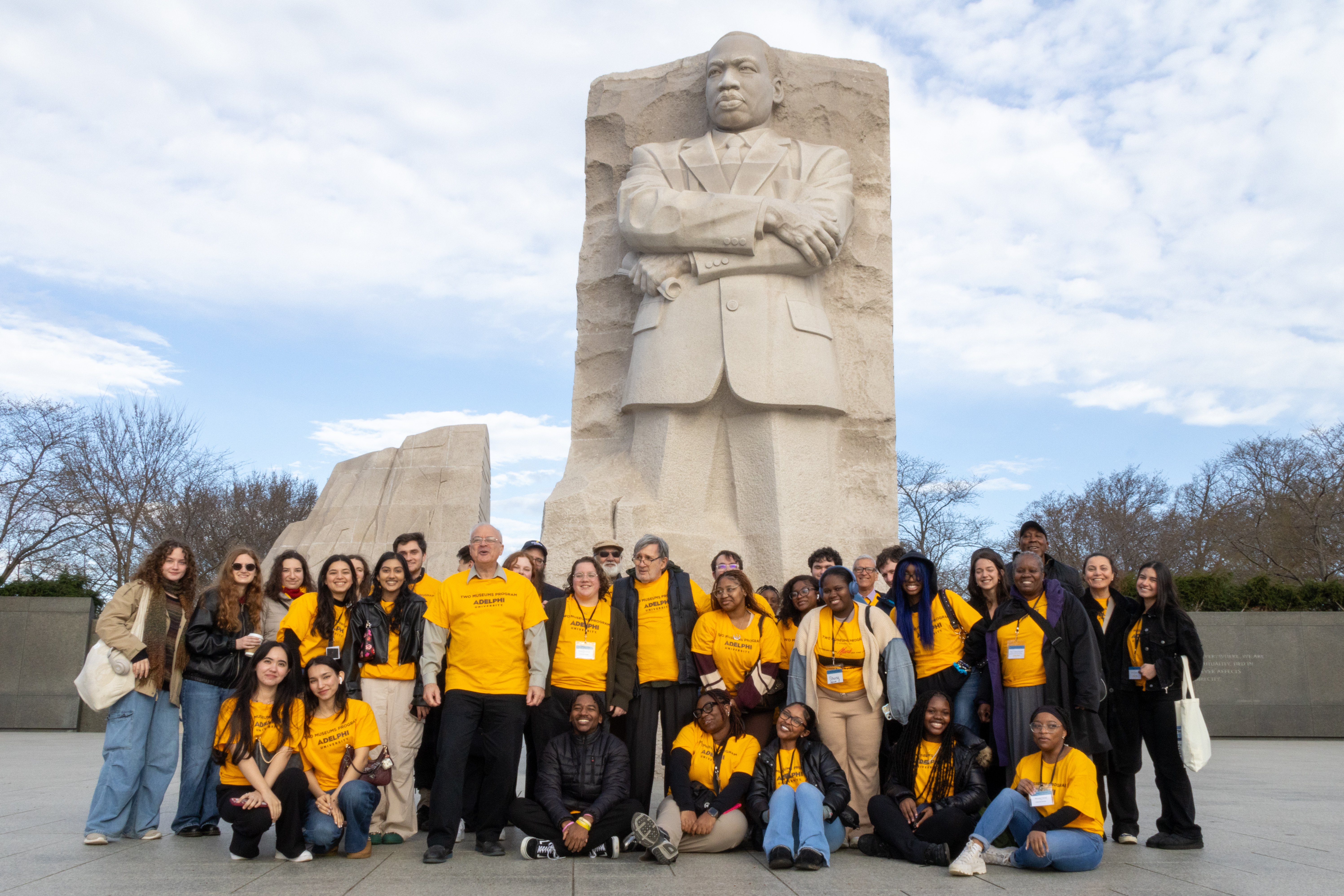 A group of about 25 students, faculty and administrators stand before the Martin Luther King Jr. Memorial.