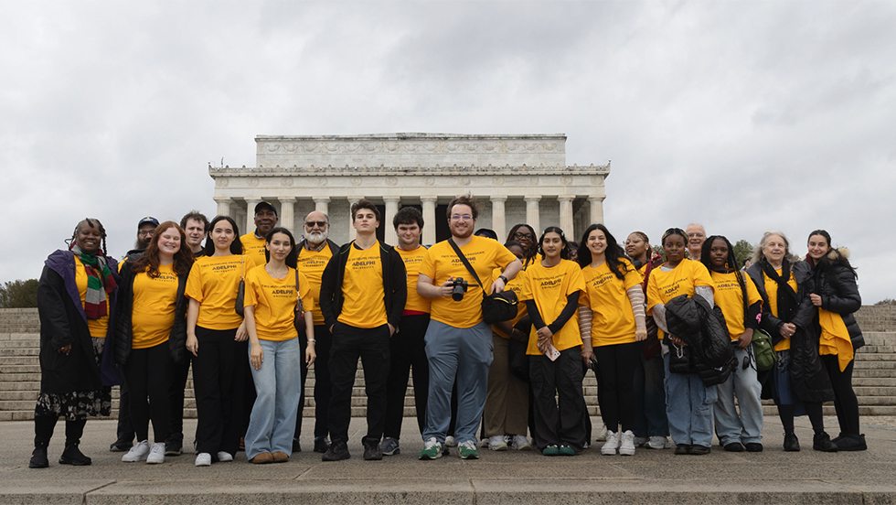 A group of about 25 students, faculty and administrators stand before the Lincoln Memorial.