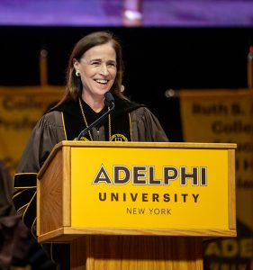 Woman smiling wearing graduation regalia at a podium