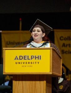 A woman wearing graduation regalia speaking at a podium