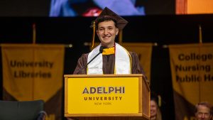 Young man wearing graduation cap and gown smiling and stadium at a podium
