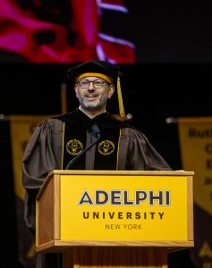 A man smiling at a podium wearing graduation regalia