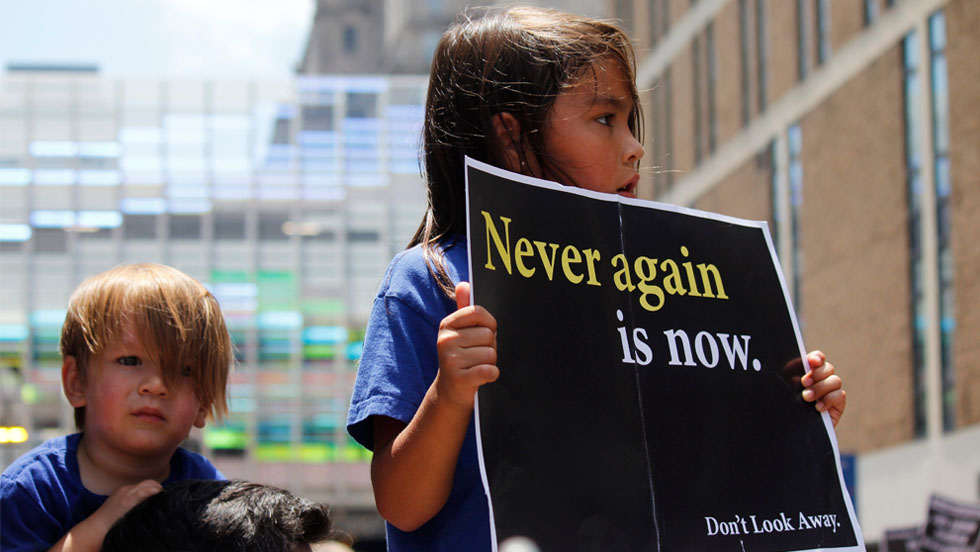 Two young children with a sign saying Never Again.
