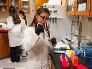 A young woman in a lab coat is focused on her work at a laboratory bench, surrounded by scientific equipment.
