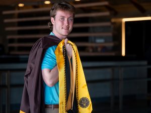 A young man in graduation gown looks confident on his Commencement day.