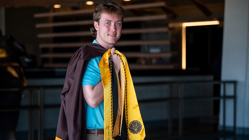 A young man in graduation gown looks confident on his Commencement day.