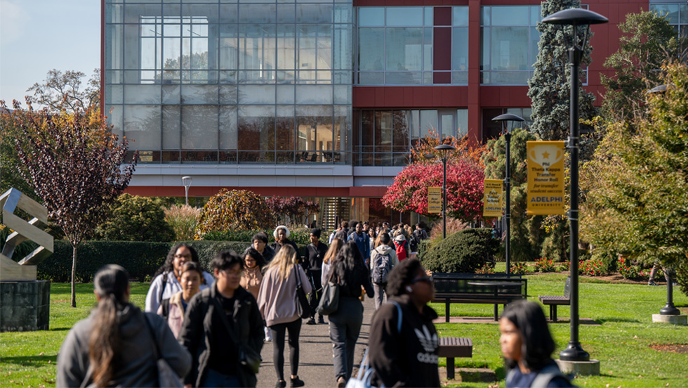 Students walk to and from class on sidewalk in front of a large modern academic building