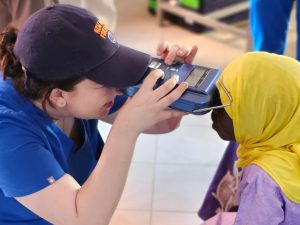 Medical student Anastasia Dakis holds an optical testing devise up to a young girl's eyes in an African village.