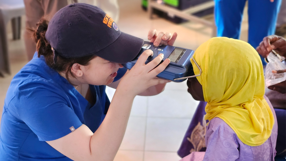 Medical student Anastasia Dakis holds an optical testing devise up to a young girl's eyes in an African village.