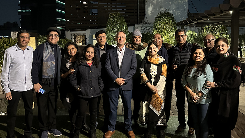 Thirteen men and women pose for a group photo outside a lovely home.