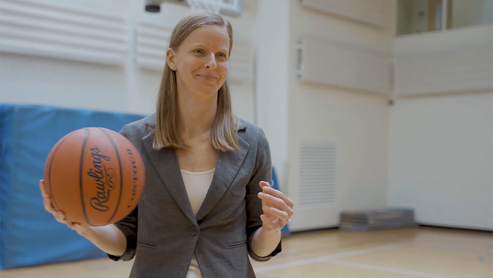 Meredith Whitley, PhD, a professor of health and sport sciences, stands in a gymnasium, holding a basketball.