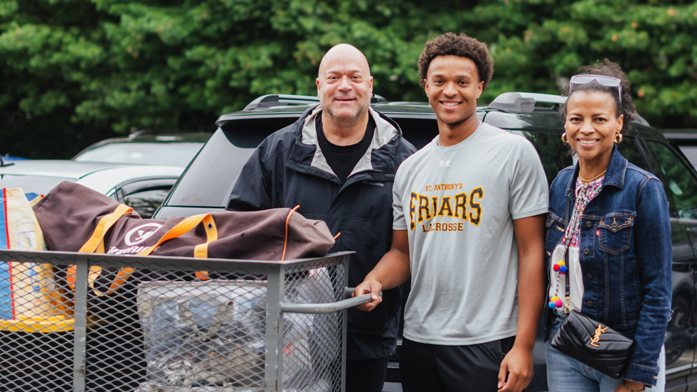 A new student pushing a large cart of belongings arrives with his mother and father.